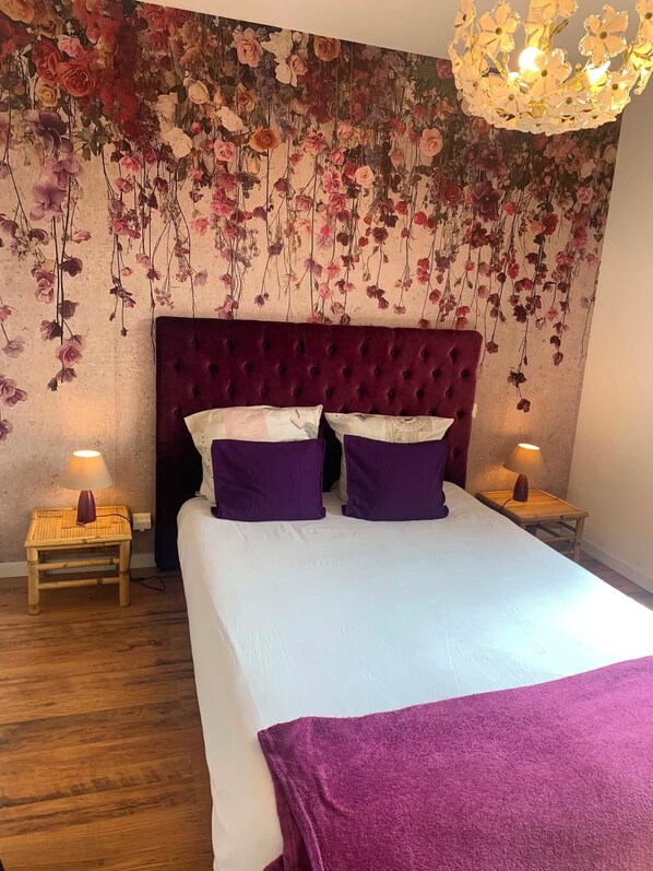 A bedroom with a tufted headboard, a large bed with white and purple bedding, and a floral wallpaper. There are two bedside tables with lamps. - Love" guest room (Corcoué-sur-Logne)