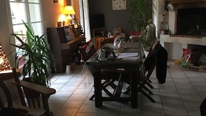 A dining area with a table set for four, surrounded by chairs. There are potted plants, a fireplace, and a television in the background. - Love" guest room (Corcoué-sur-Logne)
