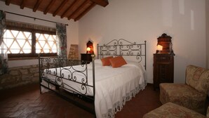 A bedroom with a wrought iron bed, a stone wall, a wooden ceiling, and a window with a lattice design.