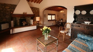A cozy living room with a stone fireplace, wooden ceiling beams, a dining area, and a blue sofa.