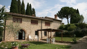 A stone building with a covered patio, outdoor seating, and a garden with trees and plants.