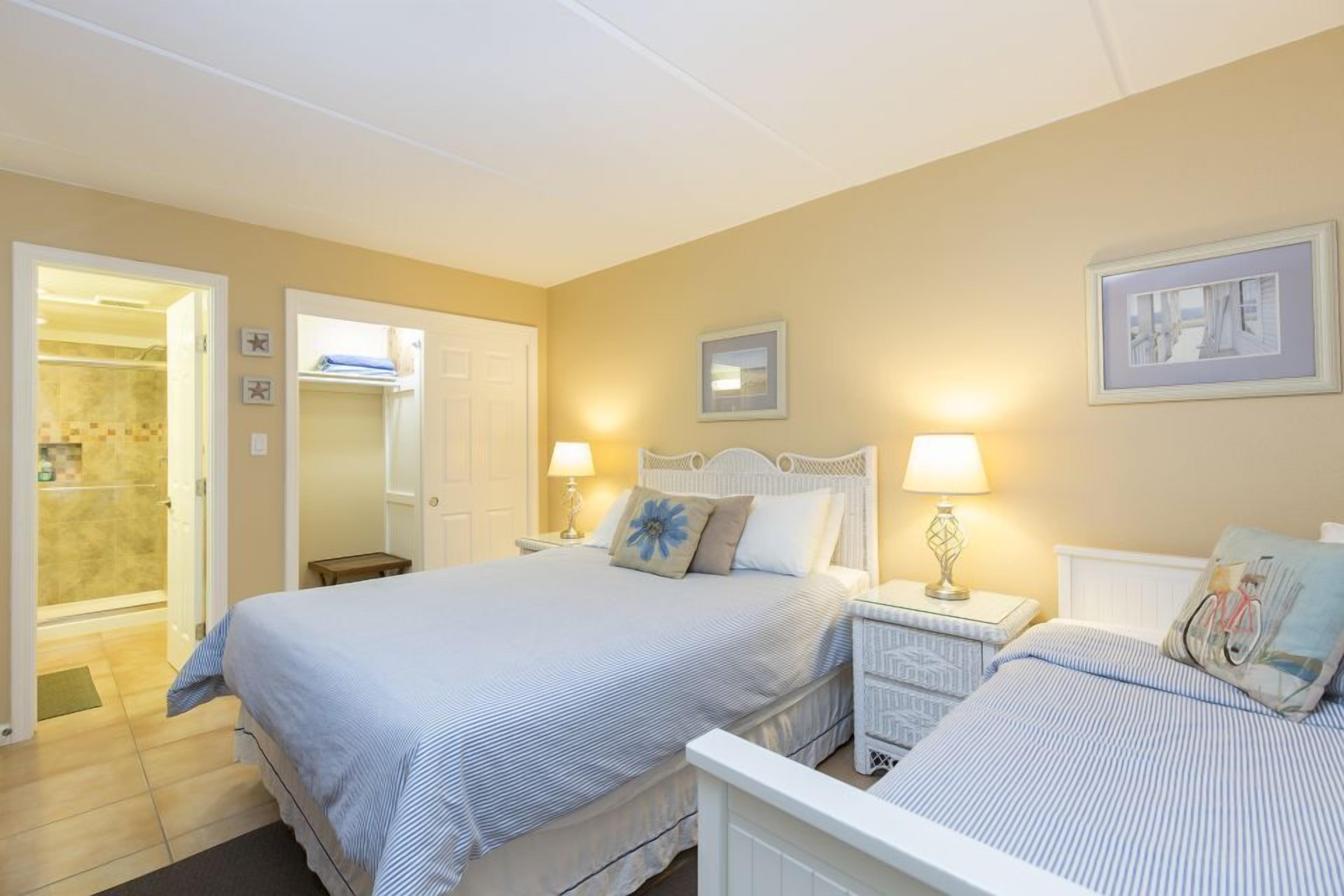 A bedroom with two beds, a bathroom, and a hallway.