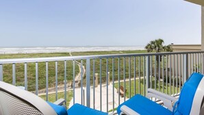 A balcony with blue chairs overlooking a beach and a road.