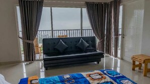 A room with a bed, a sofa, and a view through large windows.