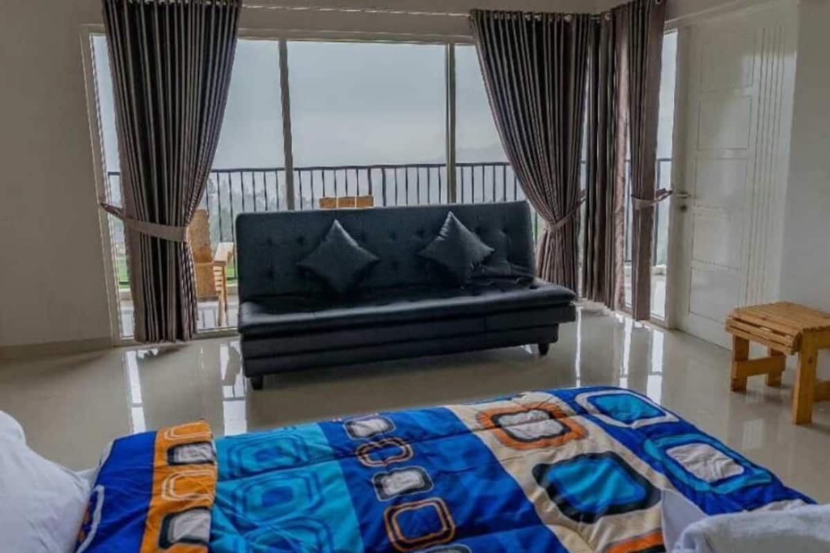 A room with a bed, a sofa, and a view through large windows.
