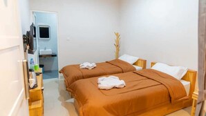 A small, clean room with two beds, a wooden desk, and a bathroom visible through an open door.