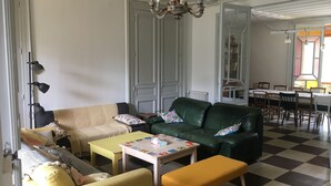 A living room with a sofa, a green armchair, a yellow armchair, a small table, and a bench. There is a chandelier hanging from the ceiling.