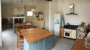 A kitchen with a wooden island, a stove, a refrigerator, and a dining area with chairs and a table.