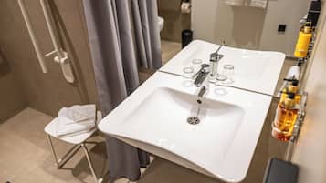 Un baño moderno con lavamanos blanco, zona de ducha y una silla pequeña.