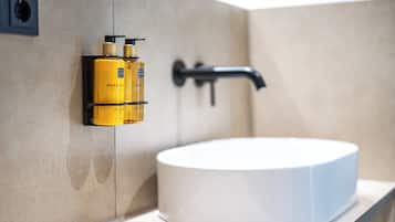 Ein Badezimmer mit einem weißen Waschbecken, einem schwarzen Wasserhahn und zwei gelben Flaschen mit Hand- und Körperseife, die an der Wand befestigt sind.