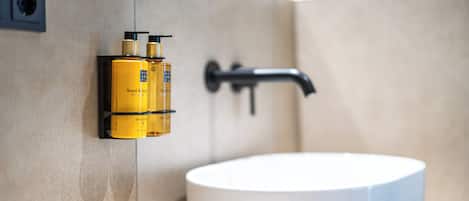 A bathroom with a white sink, a black faucet, and two yellow hand and body wash bottles mounted on the wall.