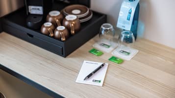 Un coin service dans une chambre d’hôtel, avec un plateau contenant des tasses, une machine à café et une bouteille d’eau.