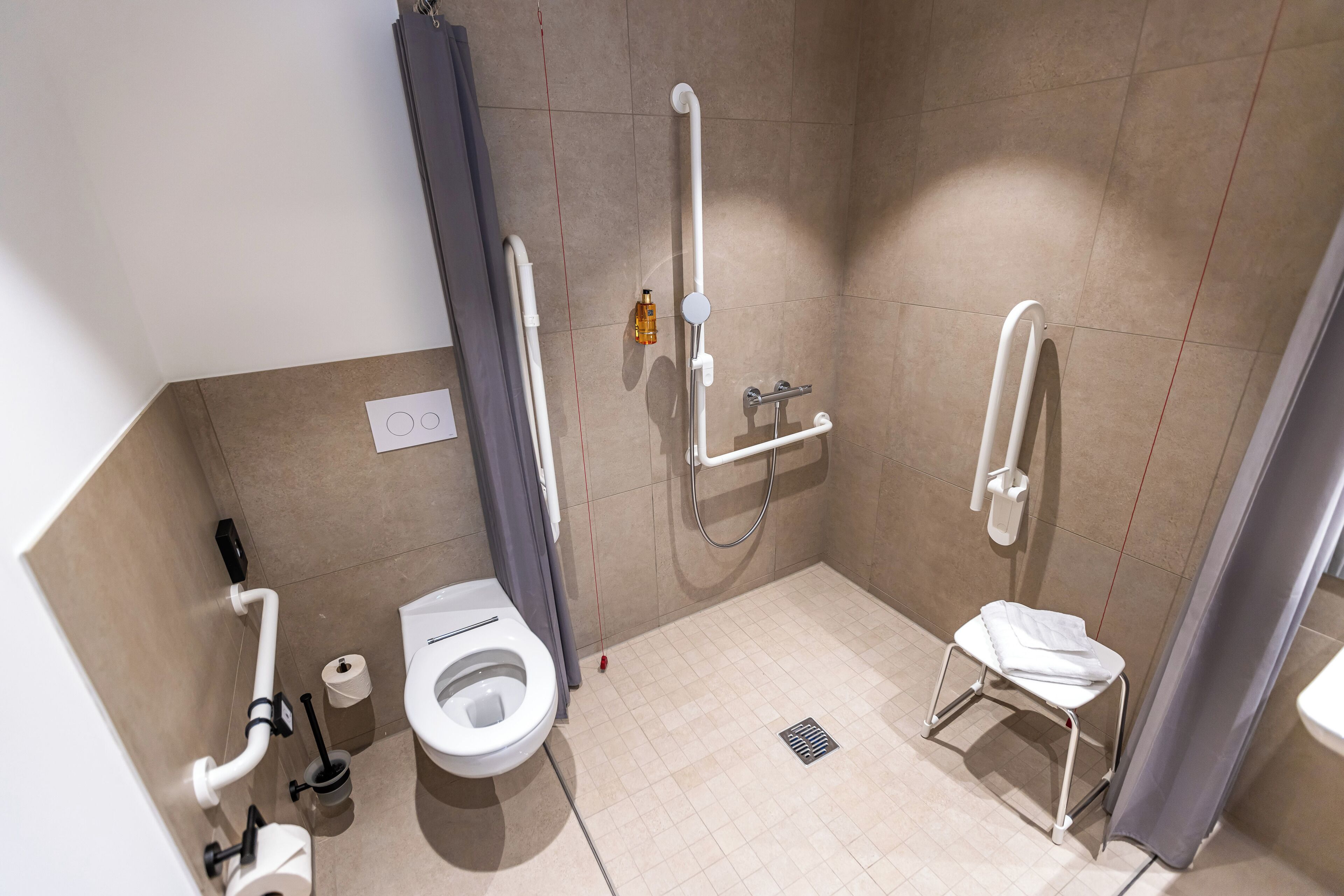 Une salle de bain moderne équipée de toilettes, d’une douche et de barres d’appui.