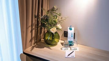 Habitación de hotel con escritorio de madera, un florero con flores, una botella de agua y un bolígrafo sobre un bloc de notas.