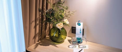 A hotel room with a wooden desk, a vase with flowers, a bottle of water, and a pen on a notepad.