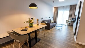 Una habitación de hotel moderna con una mesa de comedor de madera, un sofá y una pequeña mesa auxiliar.