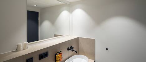 Un baño moderno con un espejo grande, un lavabo blanco y luces empotradas en el techo.