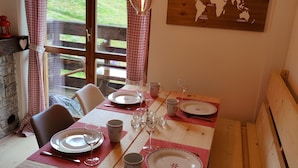 Un coin repas avec une table en bois dressée pour quatre personnes, une carte du monde accrochée au mur et une vue sur un paysage verdoyant par la fenêtre.