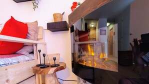 Une pièce chaleureuse avec un lit, une petite table en bois et un grand miroir qui reflète le feu.