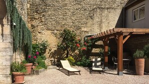 Un área de estar al aire libre con techo, un fondo de pared de piedra, plantas en macetas y una pérgola de madera.
