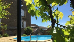 Una terraza de madera con piscina, rodeada de vegetación y edificios.