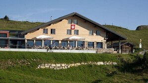 Un edificio con bandera suiza, mesas al aire libre y fachada de piedra.