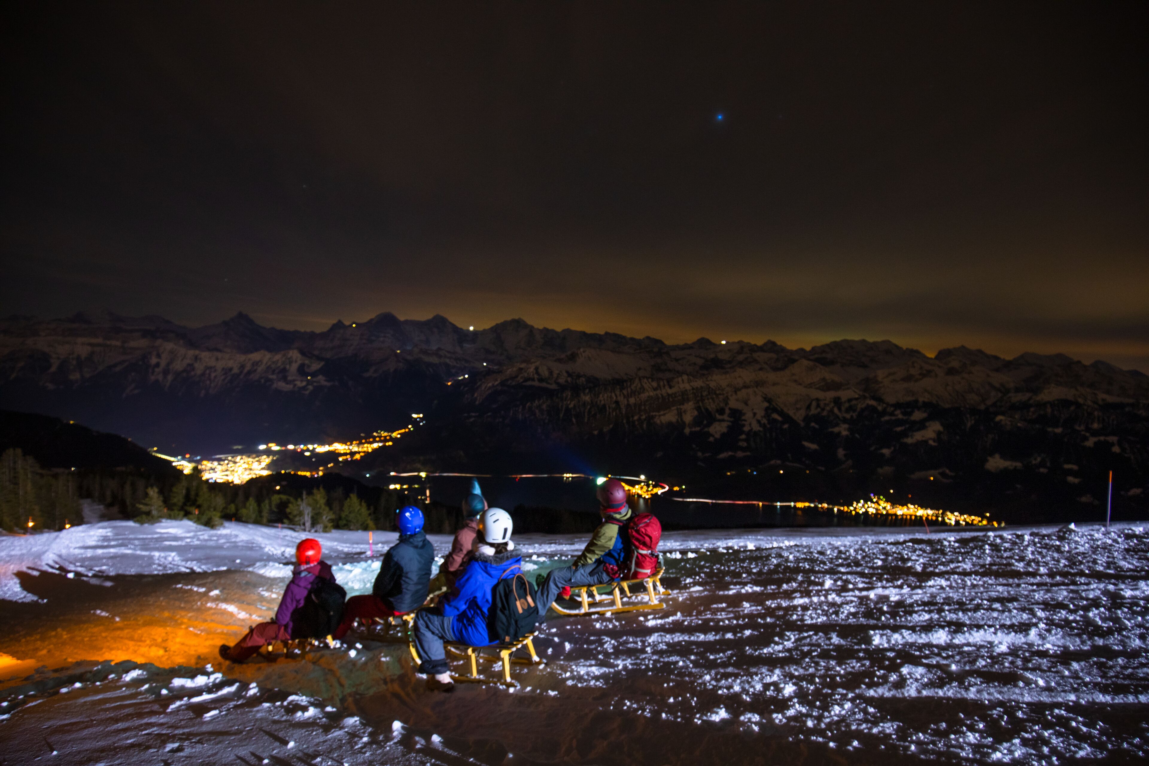 Un grupo de personas en trineos en un paisaje nevado de noche, con montañas al fondo.