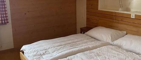 Ein Zimmer mit Holzboden und geneigtem Dach, einem Bett mit weißer Bettwäsche und einem kleinen Nachttisch.