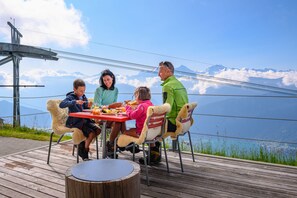 A group of people dining at a wooden table with a scenic mountain view in the background. - Berghaus Niederhorn (Beatenberg)