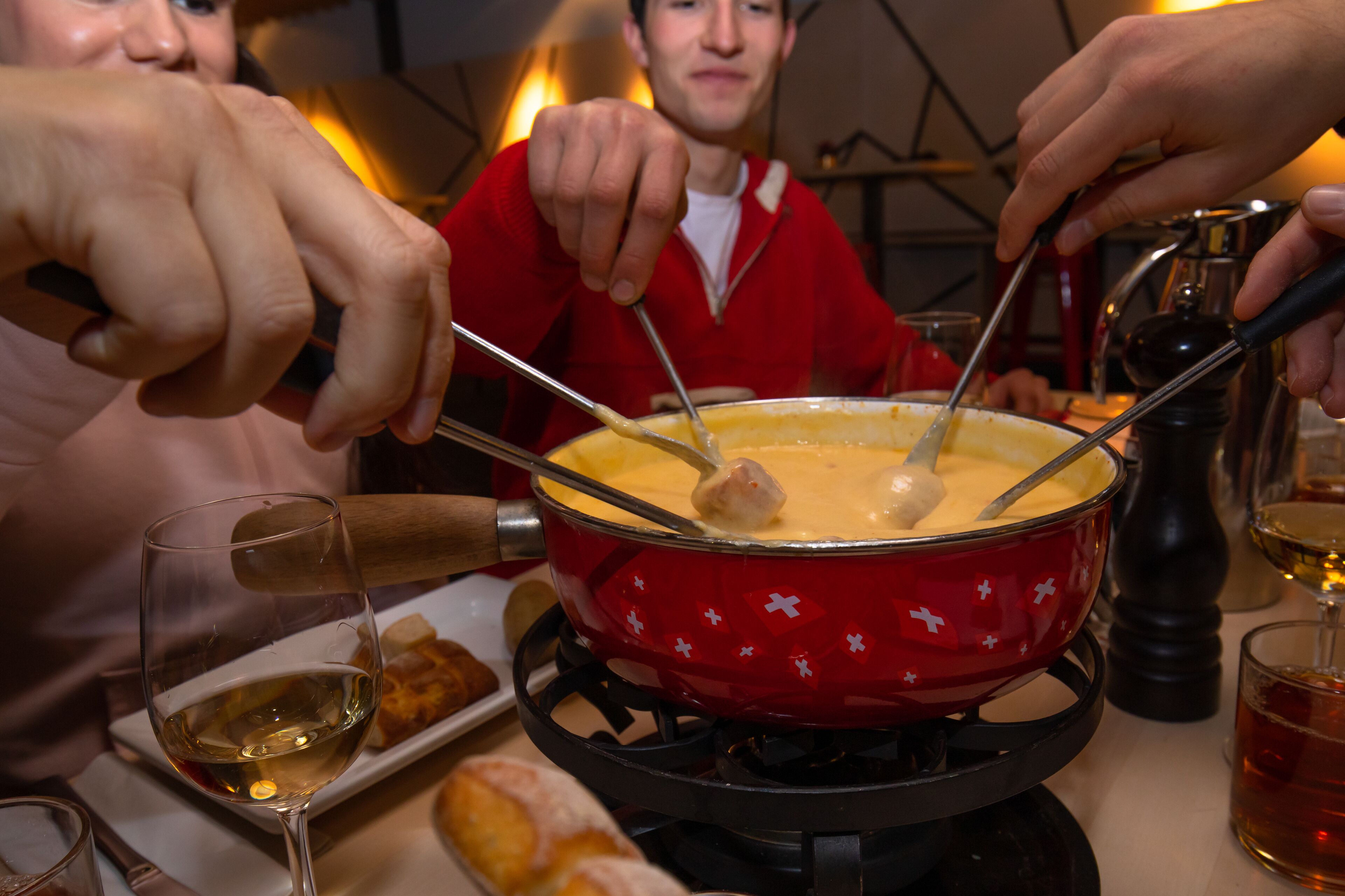 Un grupo de personas disfrutando de una cena de fondue con una olla roja sobre una estufa portátil.