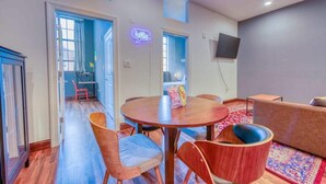 A modern living room with a round wooden table, two wooden chairs, a sofa, and a neon 'hello' sign. - Sosuite | 2BR Apt w W/D, Gym, On-SIte Restaurant (Philadelphia)