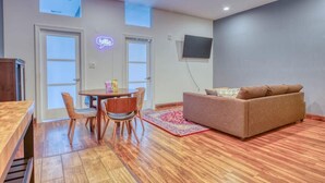 A living room with a sofa, a dining table with chairs, a TV mounted on the wall, and a neon sign. - Sosuite | 2BR Apt w W/D, Gym, On-SIte Restaurant (Philadelphia)