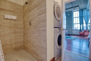 Une salle de bain avec douche, un lave-linge et une vue sur un salon comprenant une chaise et une table.