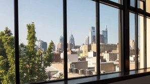 A view through large windows of a cityscape with various buildings, including a distinctive skyscraper. - Sosuite | 2BR Apt w Balcony, W/D, Gym, On-Site Bar (Philadelphia)