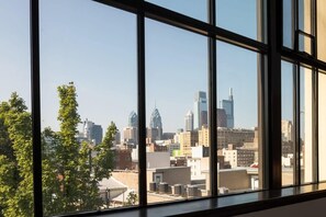 A view through large windows of a cityscape with various buildings, including a distinctive skyscraper. - Sosuite | 2BR Apt w Balcony, W/D, Gym, On-Site Bar (Philadelphia)
