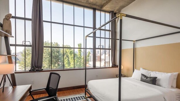 A room with a bed, a desk, a chair, and large windows. - Sosuite | 2BR Apt w Balcony, W/D, Gym, On-Site Bar (Philadelphia)