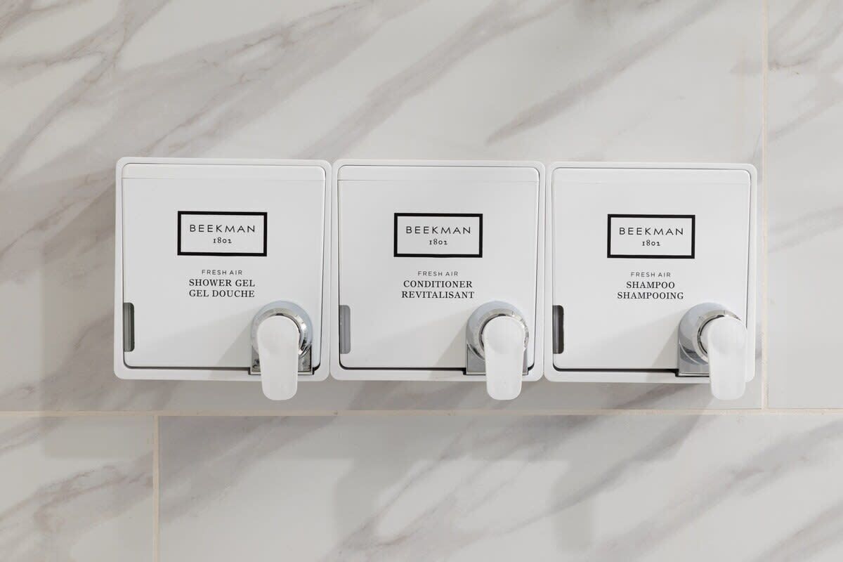 Three white dispensers labeled 'BEEKMAN' with different product names: 'FRESH AIR SHOWER GEL', 'FRESH AIR CONDITIONER REVITALISANT', and 'FRESH AIR SHAMPOO SHAMPOOING'.
