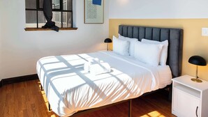 A neatly made bed with white linens, a grey upholstered headboard, and a bedside table with a lamp. - Sosuite | 2BR Apt w Balcony, W/D, Gym, On-Site Bar (Philadelphia)