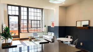 A modern interior with a large window, a white sofa, a glass coffee table, and a small dining table. - Sosuite | 2BR Apt w Balcony, W/D, Gym, On-Site Bar (Philadelphia)