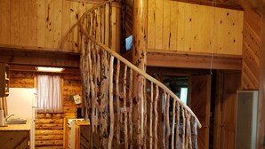 A rustic wooden interior with a spiral staircase, a kitchen area, and a bed with floral bedding. - Circle Pine Ranch-"The Real Log Cabin Experience" (Alpine)