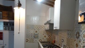 Uma cozinha compacta com fogão a gás, forno embutido e geladeira. Possui um painel de backsplash estampado e uma luminária pendente.
