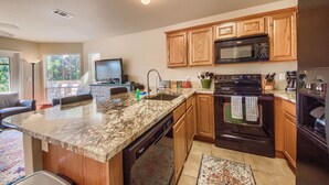 A modern kitchen with granite countertops, wooden cabinets, a built-in microwave, and a dishwasher. - Dreams And Streams Ww H303 3 Bedroom Condo by RedAwning (New Braunfels)