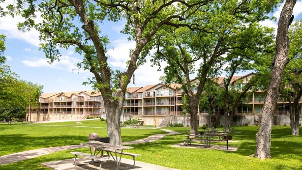 A courtyard with picnic tables and a building with multiple balconies. - Dreams And Streams Ww H303 3 Bedroom Condo by RedAwning (New Braunfels)