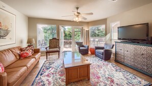 A living room with a brown leather couch, a glass coffee table, and a patterned rug. There is a television on a cabinet, and a ceiling fan. - Dreams And Streams Ww H303 3 Bedroom Condo by RedAwning (New Braunfels)