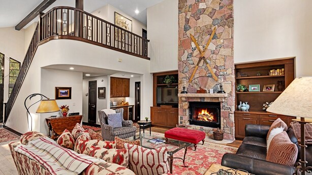 A spacious living room with a fireplace, a staircase, and a kitchen in the background. - Enclave 158 4 Bedroom Home by RedAwning (Avon)