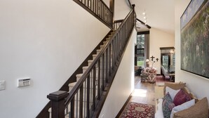 A spacious hallway with a wooden staircase, a large painting, and a cozy seating area with a patterned rug. - Enclave 158 4 Bedroom Home by RedAwning (Avon)