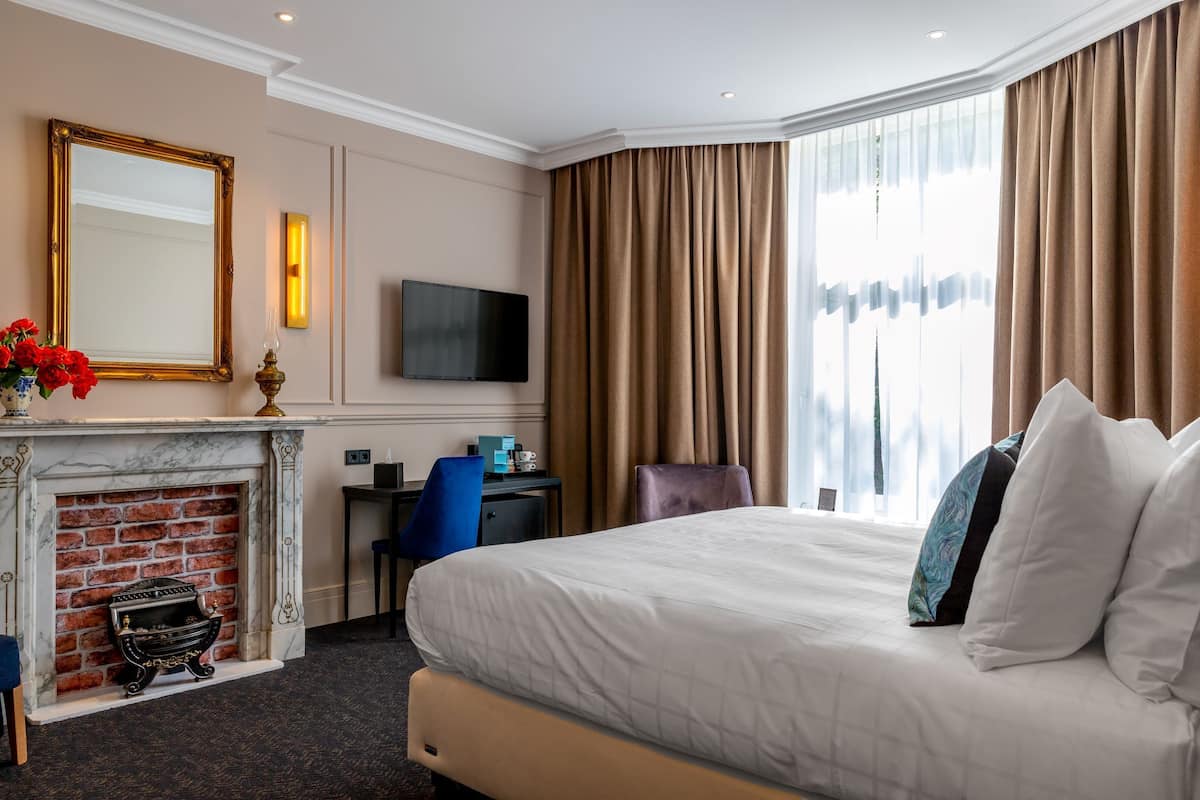 Hotelkamer met een groot bed, een flatscreen televisie aan de muur, een open haard, een bureau met stoel en een groot raam met gordijnen.