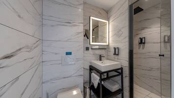 Un baño moderno con paredes de mármol, un lavabo blanco, un espejo y una cabina de ducha de vidrio.