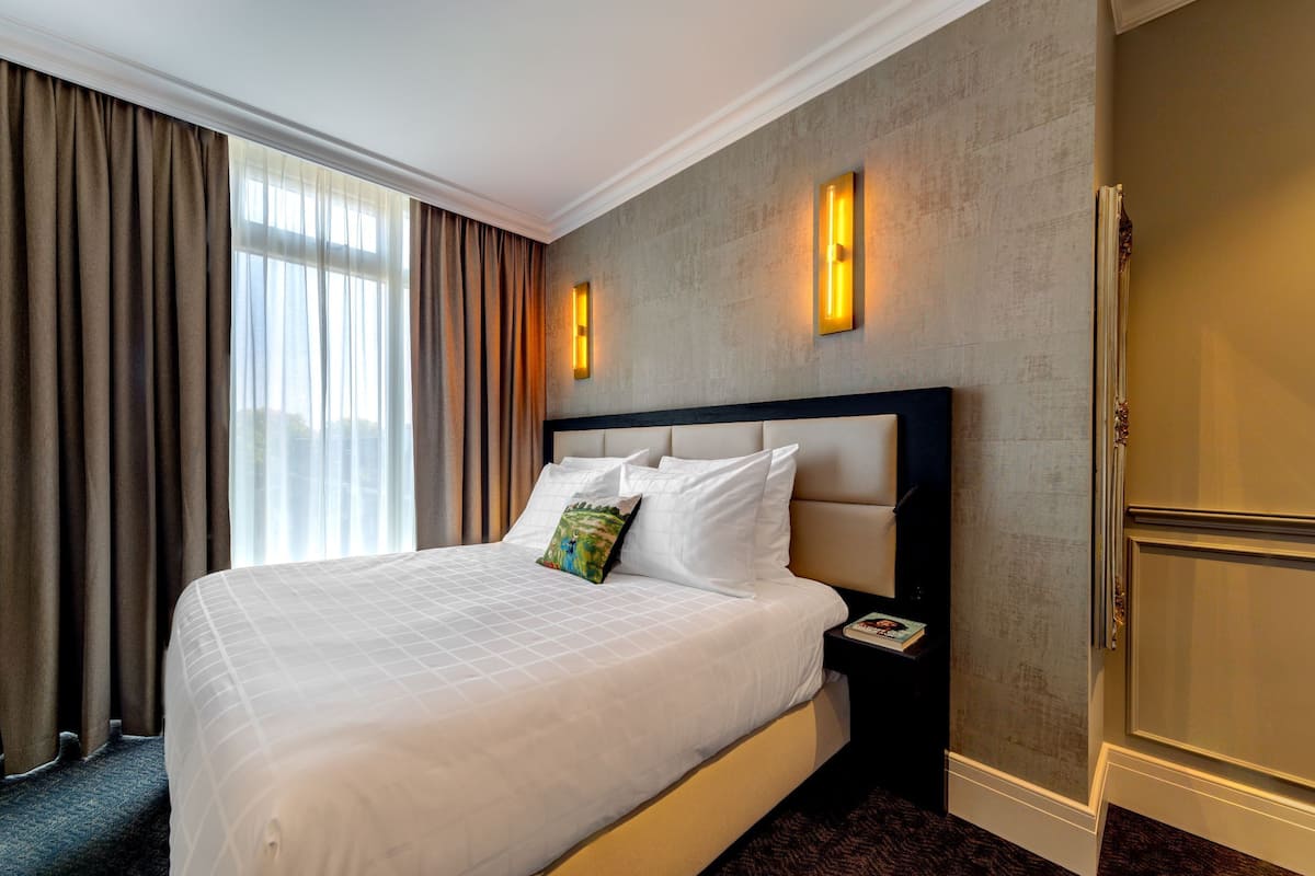 Een hotelkamer met een groot bed, een nachtkastje, een wandlamp en uitzicht op het omliggende landschap.