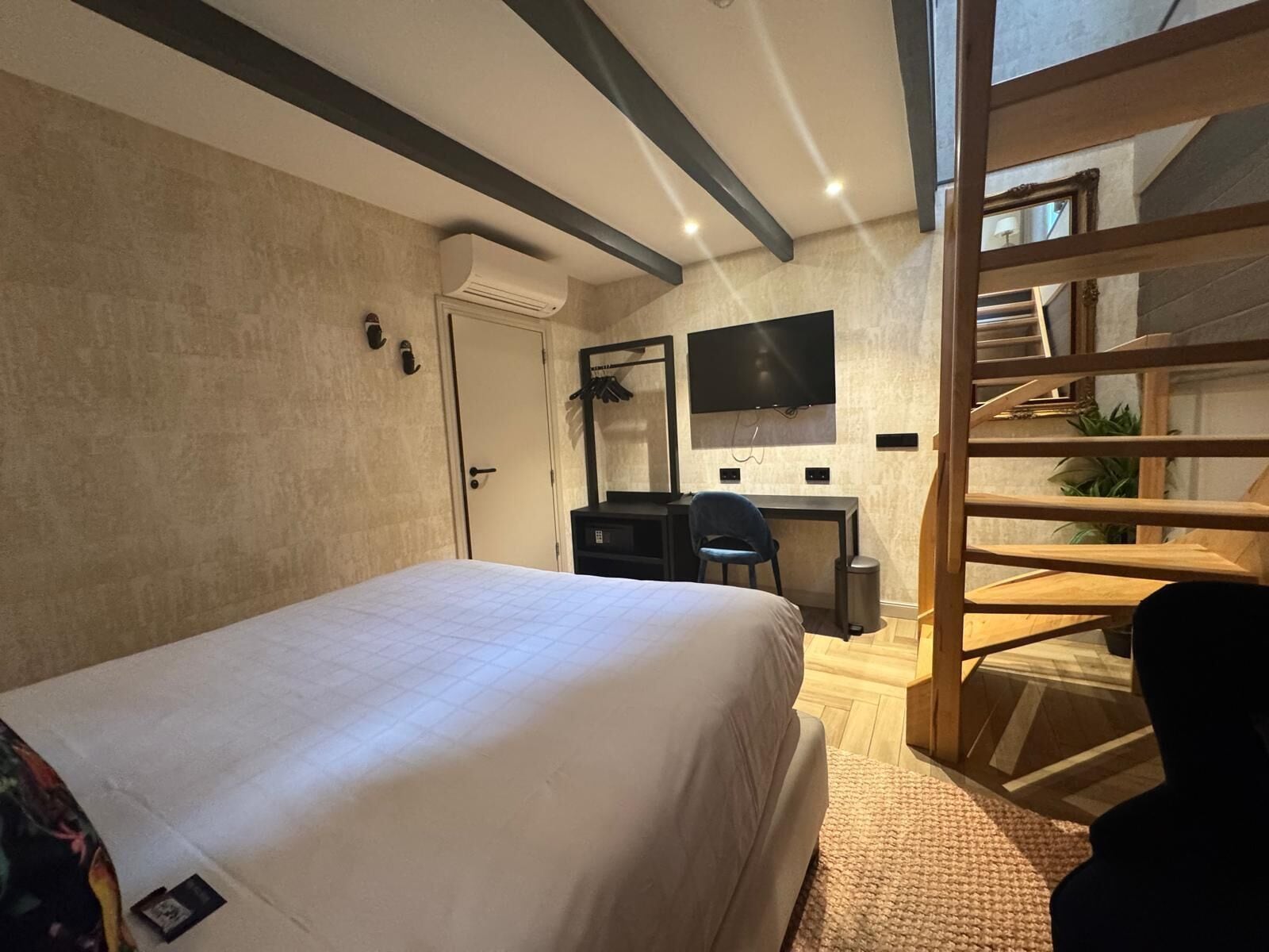 Quarto de hotel com cama, escrivaninha, cadeira, televisão e escada.